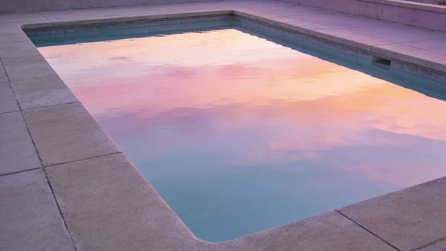 Sunset reflection in minimalist rectangular pool with pastel sky and concrete deck
