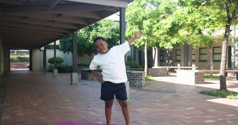 African american schoolboy balancing on mat in sunny school courtyard practicing stretching