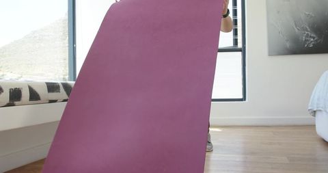 African woman holding purple yoga mat in minimalist bedroom wearing sneakers and watch