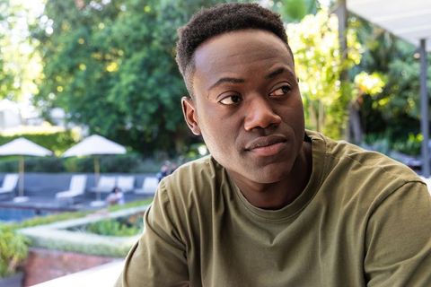 Contemplative african man sitting on pool deck looking right in sunlit garden portrait