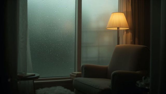 Cozy armchair by rainy window with warm lamp light, moody intimate interior