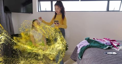 Teen friends applying makeup with golden glitter overlay in bright modern bedroom