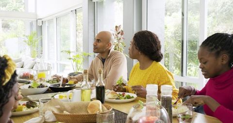 Diverse multigenerational family sharing bright sunlit meal around modern dining table