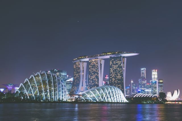 Majestic view of Singapore's Marina Bay at night, showcasing the illuminated skyline with iconic architectural structures and the reflection on the water. This image is ideal for use in travel brochures, tourism advertisements, architectural features, and articles about urban living or Asian cities.