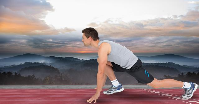 This image features a male athlete in a starting position on a running track with a scenic mountain sunset background. Ideal for use in sports promotions, fitness advertisements, motivational posters, and articles on athletic training and outdoor activities.