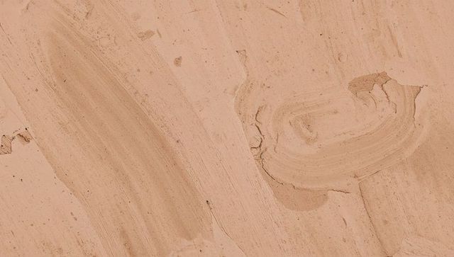 Beige plaster wall featuring broad trowel strokes, circular swirl patch, chipped stucco