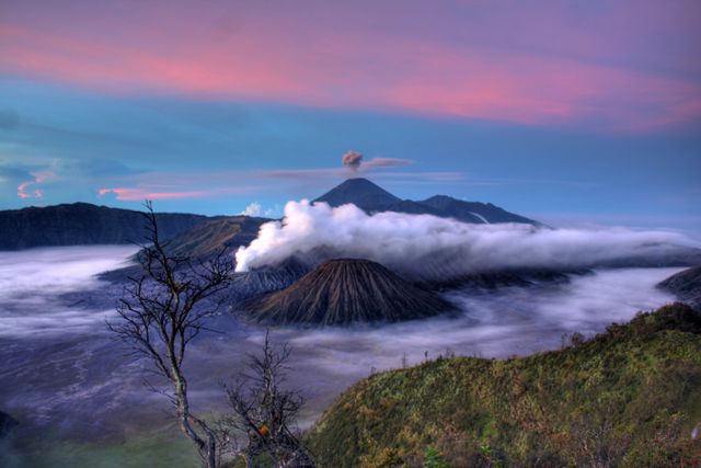 Mount Bromo surrounded by mist and clouds at sunrise in East Java, Indonesia. This captivating nature scene with a smoking volcano is ideal for travel promotions, adventure-themed content, and nature photography collections.
