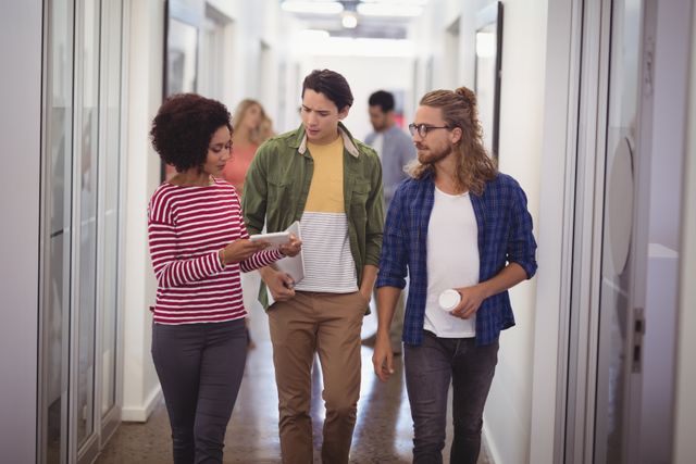 Diverse business team walking through office corridor, engaged in discussion. Ideal for illustrating teamwork, collaboration, and modern workplace environments. Suitable for corporate websites, business presentations, and articles on professional communication.