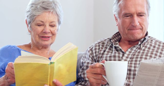 Senior couple enjoys a relaxed moment at home, woman reading a book while man drinking coffee and reading newspaper. Perfect for themes of retirement, simple lifestyle, family moments, and aging gracefully.