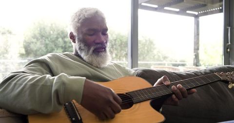 Elderly Man Relaxing at Home Playing Acoustic Guitar