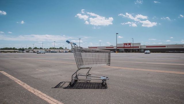 Lonely shopping cart sitting in empty supermarket parking lot under blue sky
