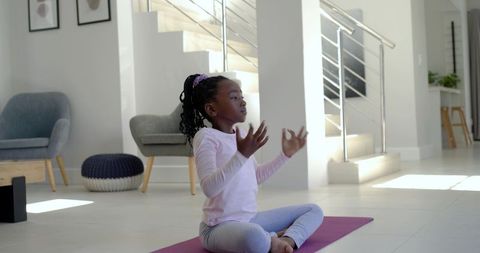 African girl practicing yoga and meditation on purple mat in sunlit modern living room