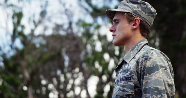 A young Caucasian male in an Air Force uniform stands outdoors, with copy space. His expression is serious, reflecting the discipline and commitment associated with military service.