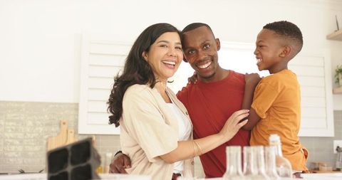 Smiling multicultural family hugging at bright modern kitchen island, joyful parenting moment