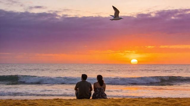 Couple watching vibrant sunset over ocean while sitting on sandy beach with seagull