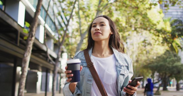 Asian woman walking using smartphone and drinking takeaway coffee - Download Free Stock Photos Pikwizard.com
