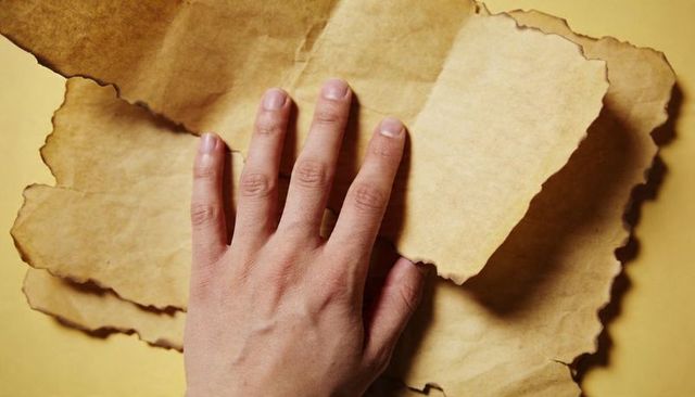 Hand pressing torn kraft paper layers on yellow backdrop, textured minimalist closeup