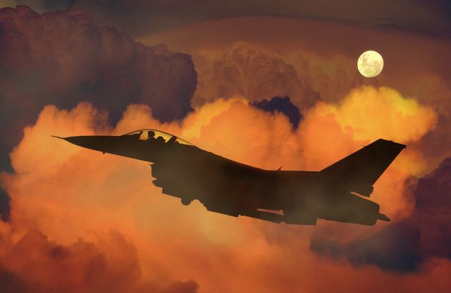 A jet fighter is flying against a colorful and dramatic sky at sunset with the moon visible in the background. The aircraft is silhouetted by the intense hues of orange, red, and purple in the sky. This image can be used for themes involving military aviation, defense technology, patriotic content, or advertisements for aviation-related products. It would also fit well in publications or websites about aerial combat, military strategy, or aerospace engineering.