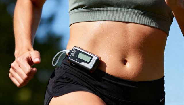 Female runner wearing portable medical pump jogging outdoors with sweaty midriff
