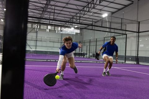 Diving duo chasing ball on indoor purple padel court during fast-paced doubles play