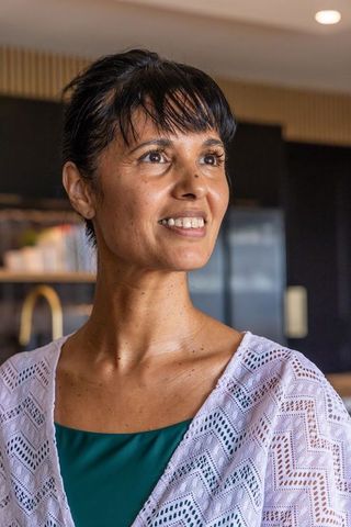 Mature african woman smiling in contemporary kitchen wearing teal top and white cardigan