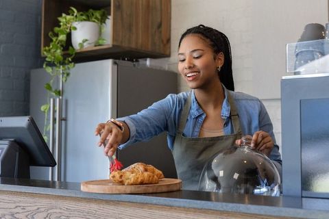 Smiling african american barista serving fresh croissants with red tongs at cafe counter