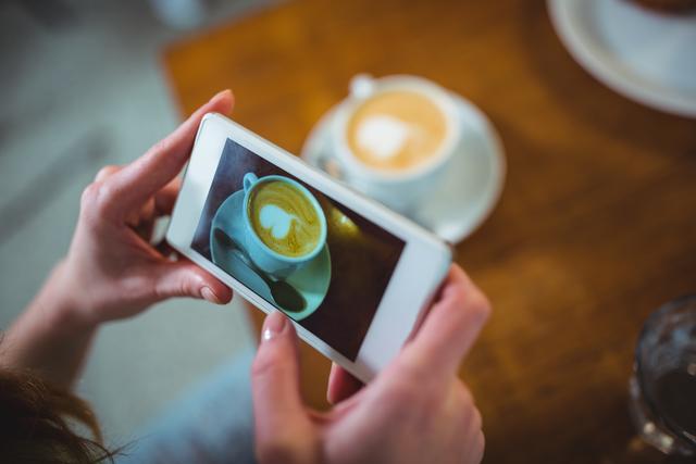 Woman clicking photo of coffee from mobile phone in cafÃ©