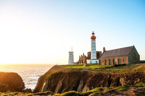 Stunning lighthouse with church overlooking cliffs at sunrise