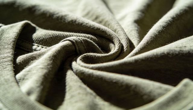Olive green knit fabric swirling spiral macro texture with visible seam and lint fibers
