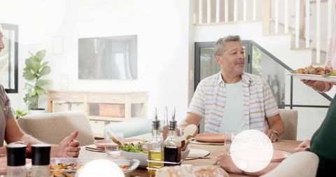 Middle-aged man reaching for roasted platter at bright casual family dinner