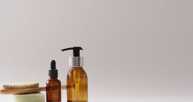 Natural amber bottles for personal care products arranged neatly with a bar of soap and a brush, against a plain light background. This minimalist composition is perfect for illustrating natural hygiene and self-care routines. Ideal for use in wellness blogs, spa advertising, and product packaging.