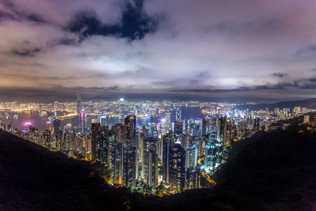 High-angle night view of Hong Kong’s illuminated skyline as seen from Victoria Peak, showcasing skyscrapers and vibrant city lights. Ideal for use in travel magazines, tourism advertisements, website headers promoting Hong Kong, or urban studies presentations.