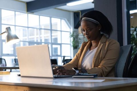 African american professional woman working on laptop at modern office desk, typing and focused