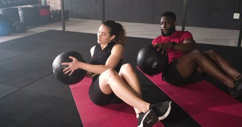 Diverse Fitness Pair Doing Russian Twists with Medicine Ball