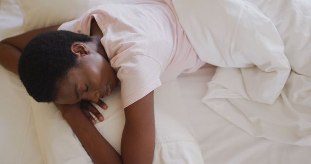 African American man sleeping peacefully on white bed sheets, illustrating rest and tranquility. The serene scene captures the comfort of sleep in a home setting. Useful for content related to health, sleep, relaxation, well-being, and lifestyle articles or advertisements promoting sleep products, bedding, and home decor.
