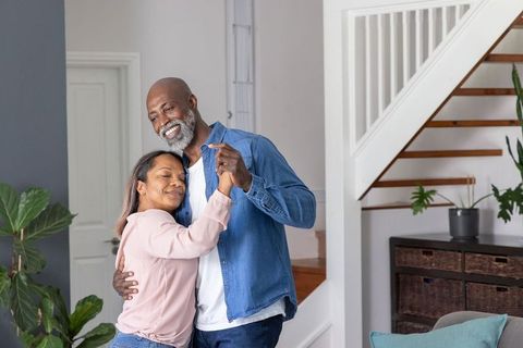 Middle-aged couple dancing and embracing in cozy modern living room near staircase, lifestyle