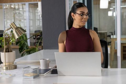 Asian professional woman working at laptop in modern open-plan office with minimalist desk