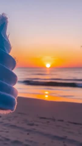 Holding glove at sunrise over ocean with sun reflection on sand vertical video
