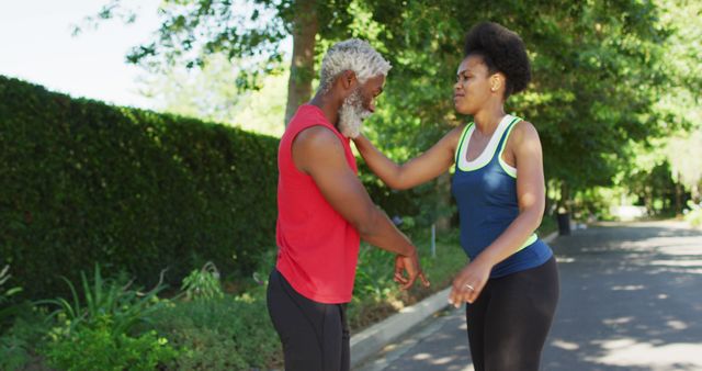 Smiling african american senior couple exercising outdoors stretching in road. healthy retirement and active lifestyle.