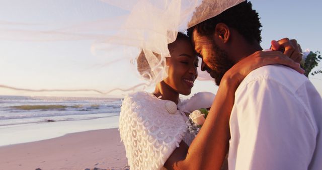 African american couple in love getting married, smiling and looking at other on the beach at sunset. marriage, love and romance, holiday by the sea.