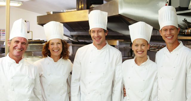 A group of professional chefs standing together in a restaurant kitchen, all smiling and wearing white uniforms with chef hats. Perfect for materials on culinary schools, restaurant promotion, team building, and hospitality industry marketing.