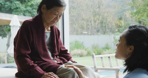 Comforting senior woman by patio door, tender home caregiving moment with natural light