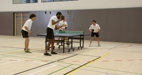 Men Engaged in Table Tennis Match in Gymnasium Setting