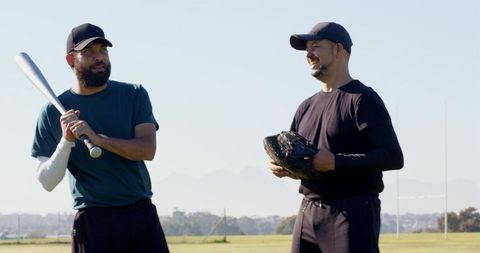 Two Men Practicing Baseball Outdoors Holding Bat and Glove Smiling Teamwork Field Moment