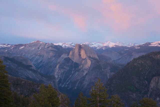 Stunning view of Yosemite National Park at sunrise showcasing the iconic Half Dome against a backdrop of majestic mountains and a pastel sky. Perfect for travel websites, nature blogs, adventure magazines, and environmental campaigns, this image portrays the beauty of natural landscapes.
