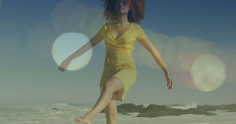 Carefree young woman walking at shore with lens flares