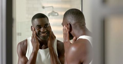 African American man smiling at mirror during morning skincare routine