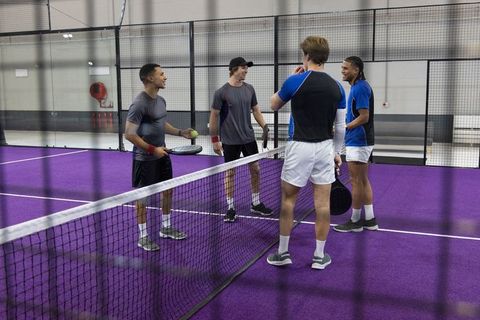 Indoor padel doubles on vibrant purple court showing teamwork and competitive warmup