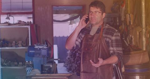 Caucasian Male Worker in Rustic Workshop Communicating on Smartphone