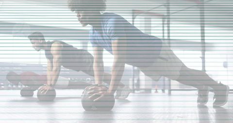 Group performing medicine-ball plank in gym training session with backlit studio light